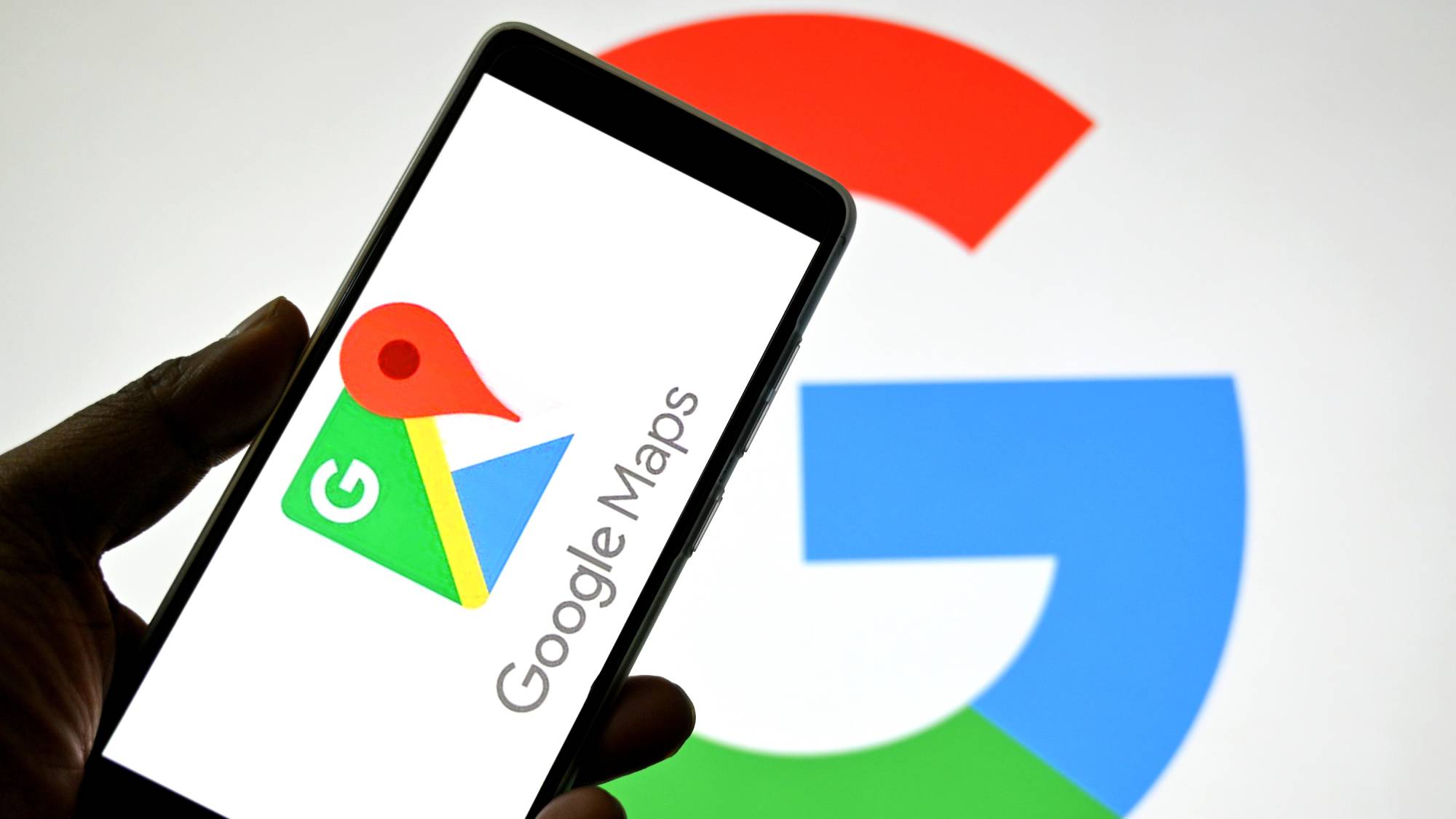 Hand holding smartphone with Google Maps app open next to the Google Maps logo