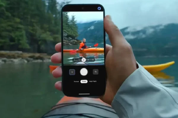 A hand holding a Google Pixel smartphone with the camera active, capturing a kayaker on a mountain lake